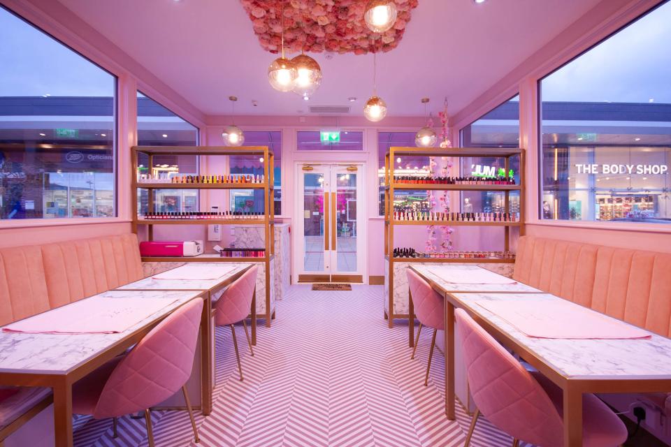 Stylish pastel pink nail salon interior featuring marble tables, plush seating, and an array of nail polishes.