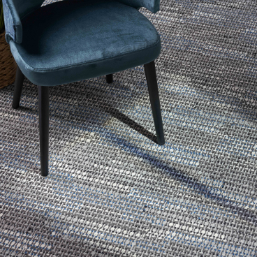 Stylish macramé design carpet featuring shades of gray and blue, paired with a modern chair and indoor plant.