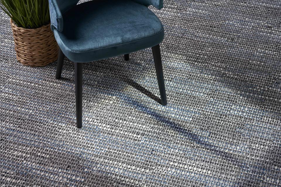 Stylish macramé design carpet featuring shades of gray and blue, paired with a modern chair and indoor plant.
