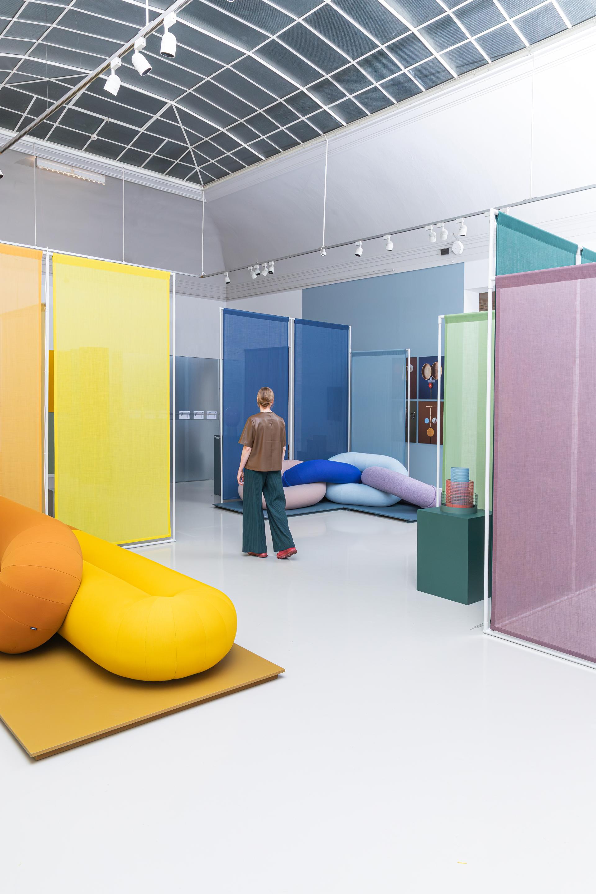 Exhibition space featuring bio-based color palettes, vibrant textile installations, and a visitor engaging with contemporary materials.