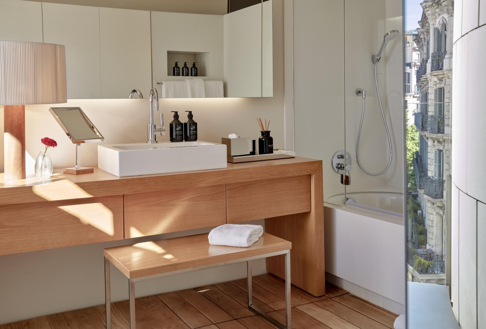 Modern hotel bathroom featuring wood accents, minimalist design, and natural light highlighting luxury toiletries in Barcelona.
