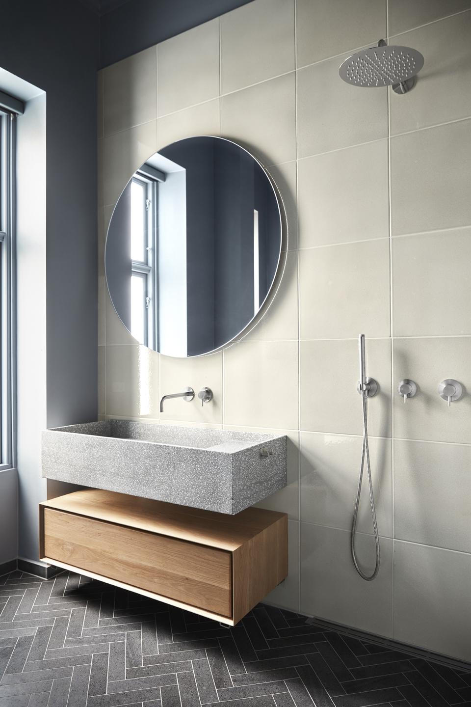 Stylish bathroom featuring a gray stone sink, round mirror, and wooden drawer, designed for an ethereal feel.