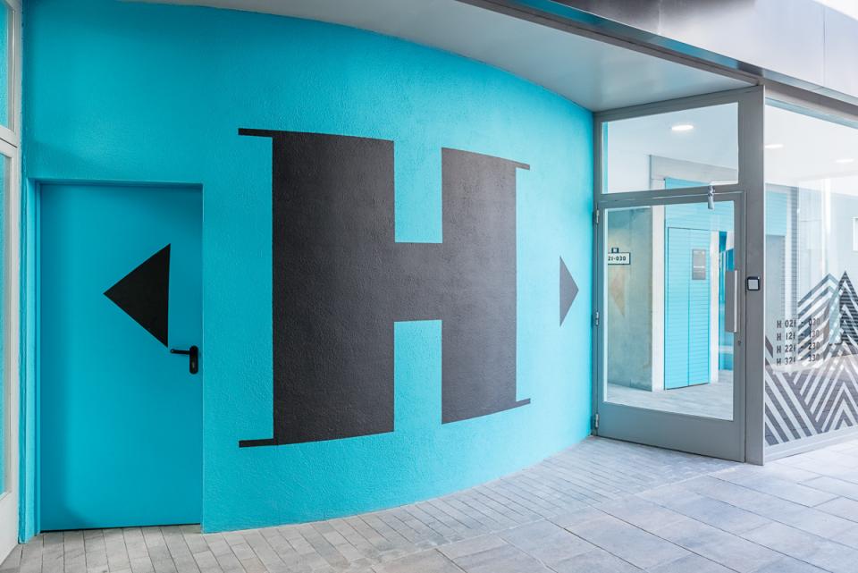 Bright turquoise wall with bold black letters and geometric shapes, showcasing the entrance design of The Student Hotel in Barcelona.