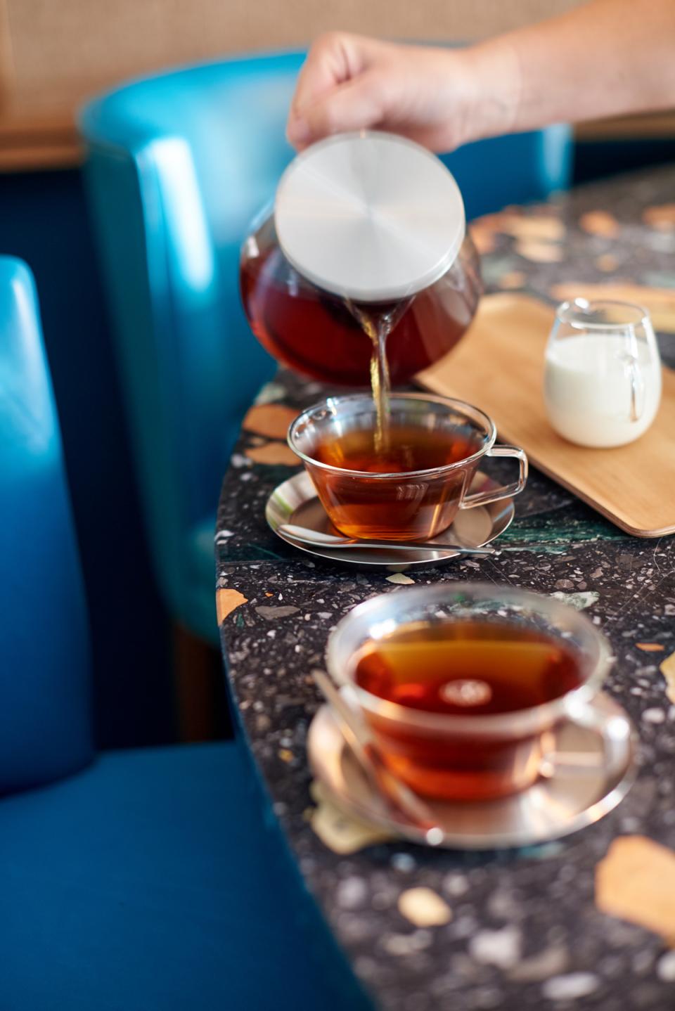 Pouring tea into glass cups on a stylish marble table, showcasing Teatulia’s elegant tea shop design.