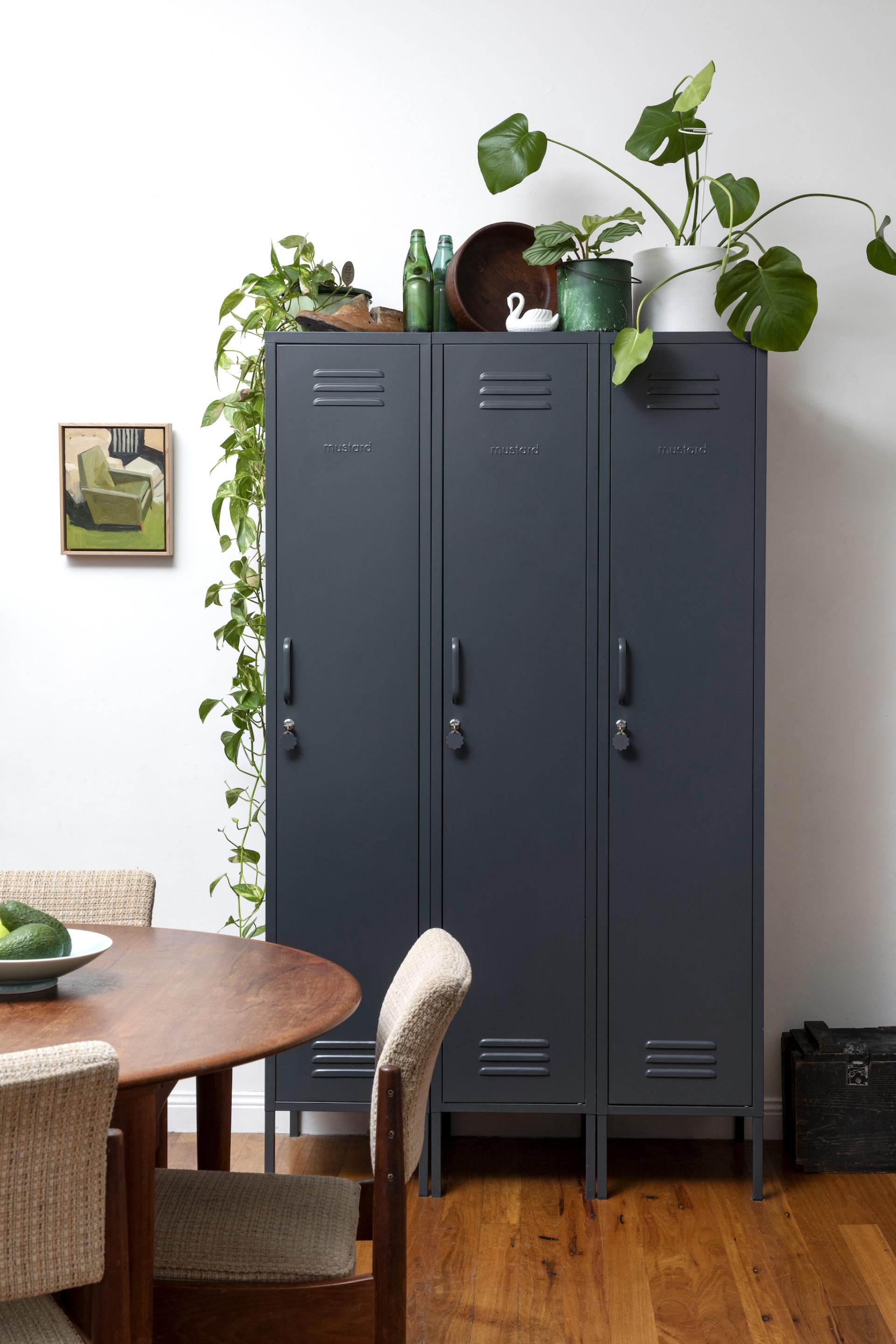 Stylish gray storage lockers adorned with plants, complementing a wooden dining table setting, reflecting Mustard Made's playful design ethos.