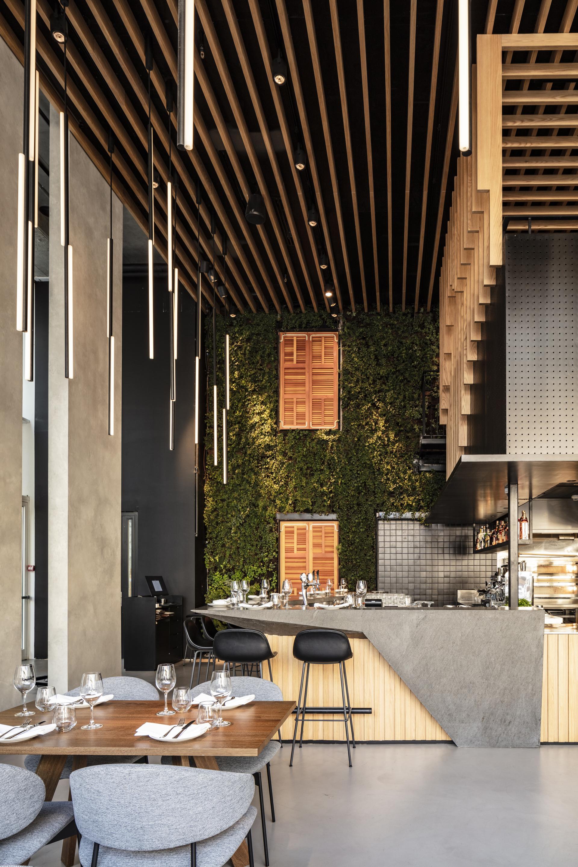 Interior of a modern Tel Aviv restaurant featuring suspended wooden beams, elegant seating, and lush green walls.