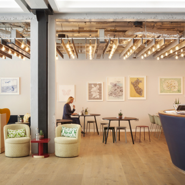 Bright and modern workspace with artwork, seating areas, and a woman working at a table, emphasizing flexible office solutions.