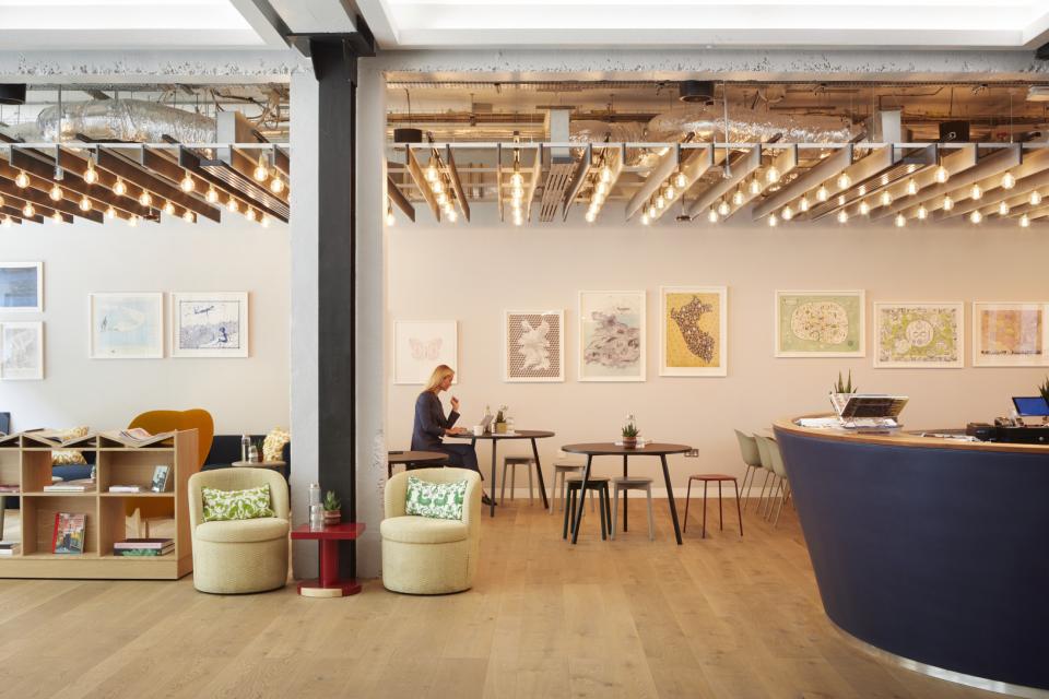 Bright and modern workspace with artwork, seating areas, and a woman working at a table, emphasizing flexible office solutions.