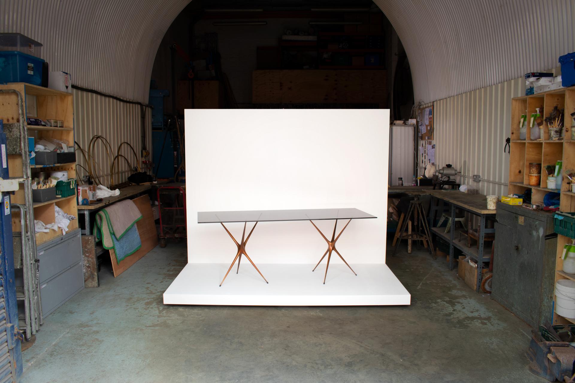 Brodie Neill's reimagined Supernova trestle table showcased in a workshop setting, highlighting its elegant design and craftsmanship.