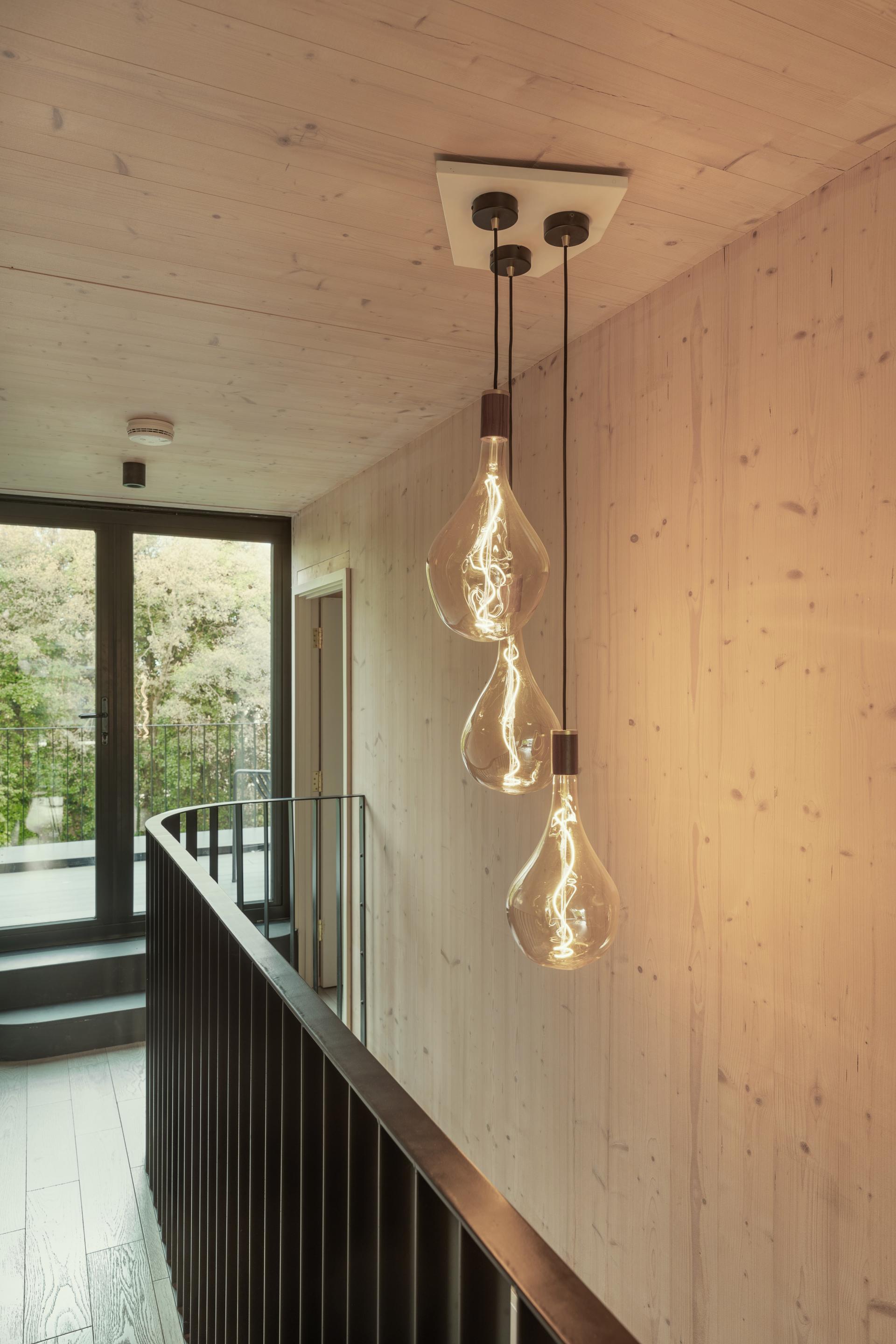 Stylish pendant lights illuminate a modern wooden hallway in the Woven residential project by Giles Miller Studio.