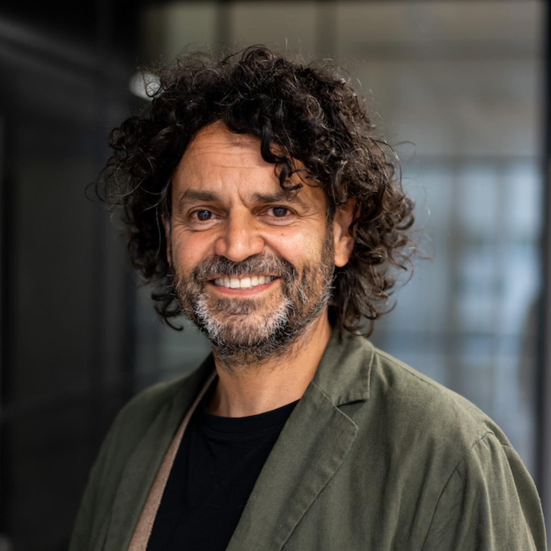 Professional man with curly hair smiling in a modern office environment, embodying the spirit of a forward-thinking workplace.