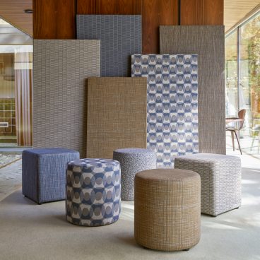Modern wool ottomans in various patterns and colors showcased against digitally printed textile panels by Camira.