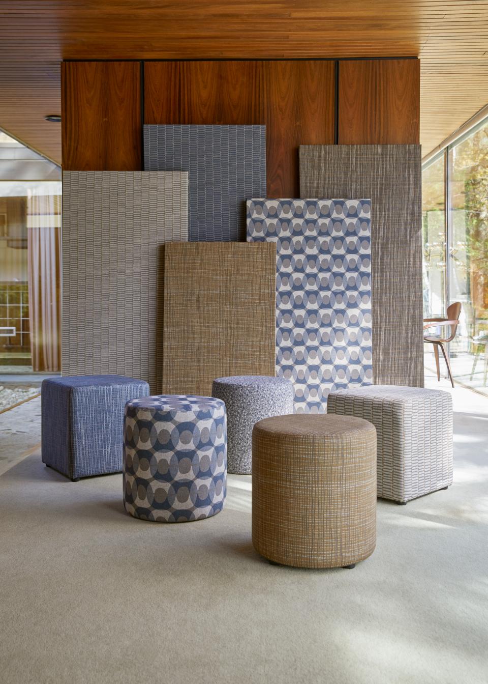 Modern wool ottomans in various patterns and colors showcased against digitally printed textile panels by Camira.