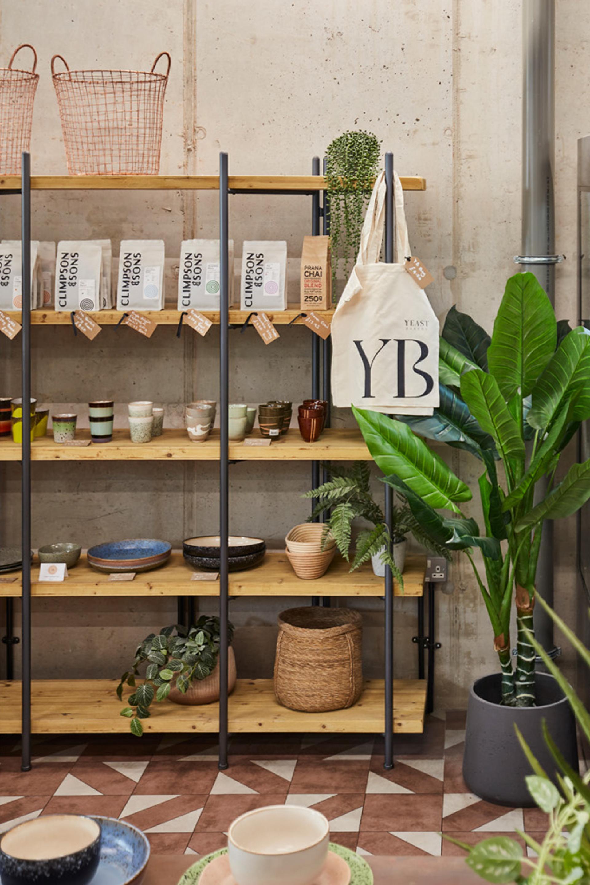 Stylish wooden shelves display unique pottery, artisanal products, and plants in Yeast Bakery's urban artisan interior.