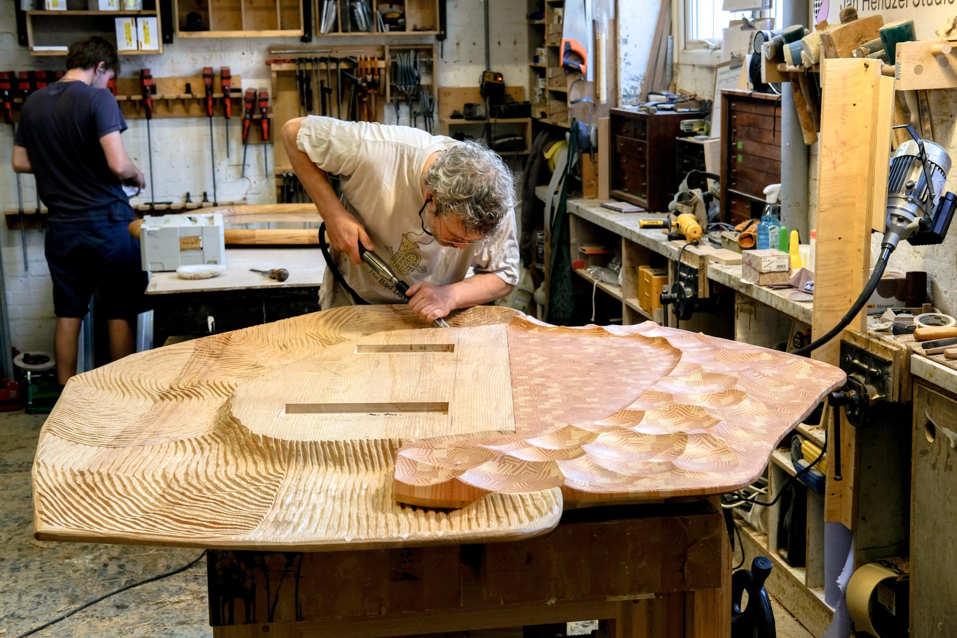 Jan Hendzel meticulously carving a large wooden sculpture in his workshop, showcasing traditional craftsmanship and innovative techniques.