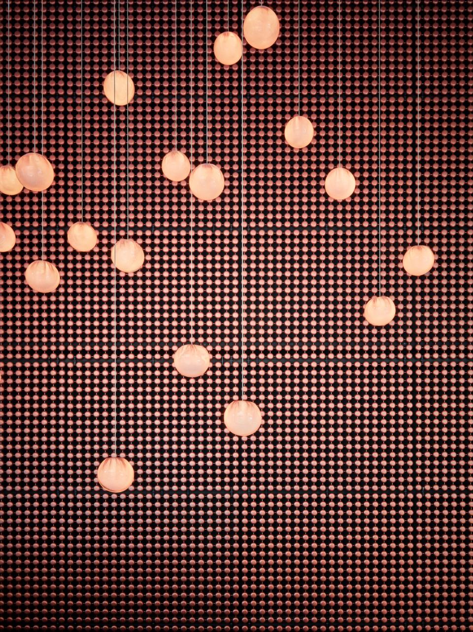 Hanging round lights illuminate a textured wall, showcasing the chic design aesthetic of Sir Victor hotel in Barcelona.