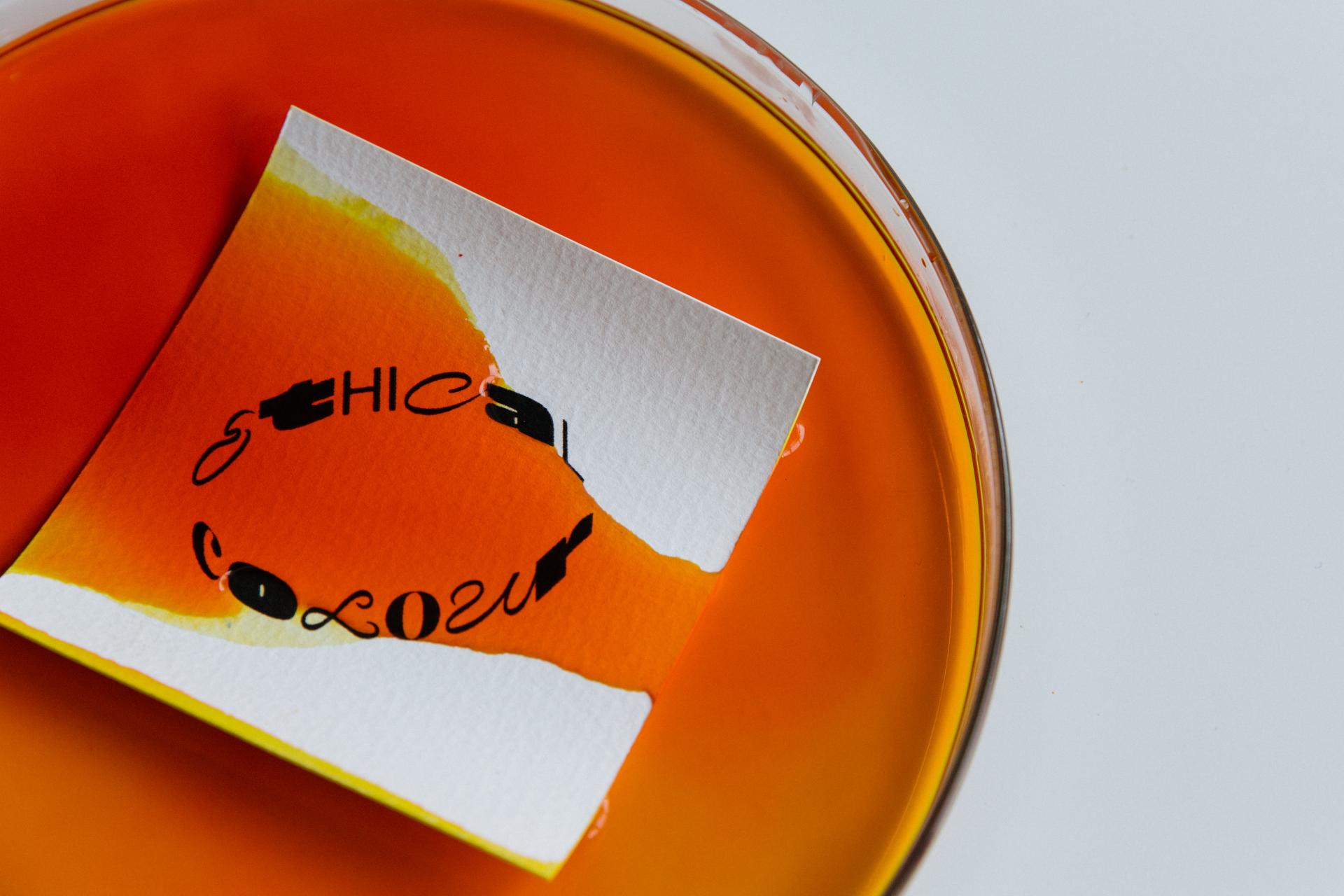 Colorful circular dye test with a white card labeled 'Ethical Colour' floating in vibrant orange liquid.