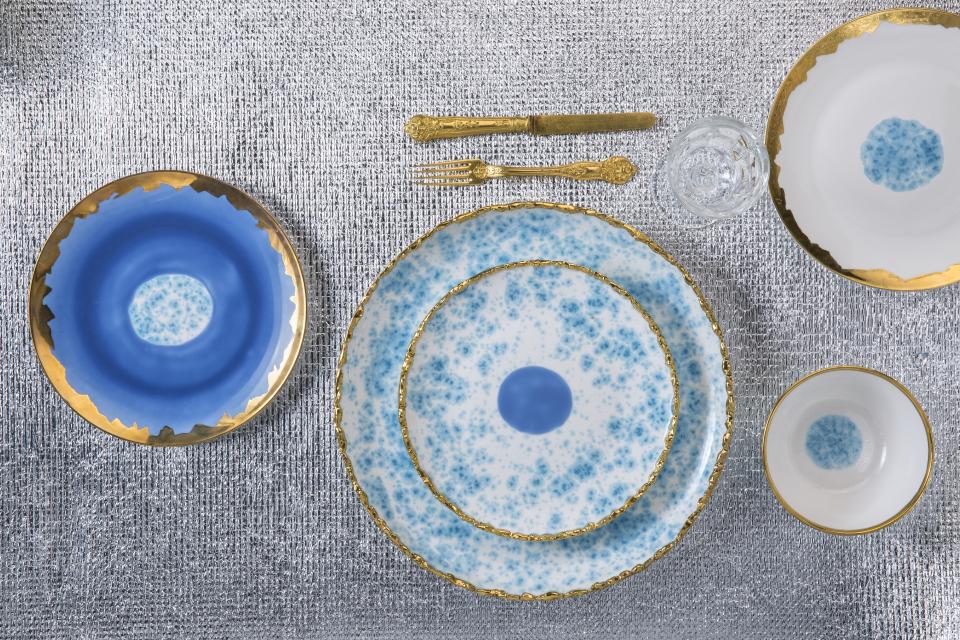 Hand-decorated ceramic and porcelain tableware by Coralla Maiuri, featuring intricate blue and gold designs on a textured background.