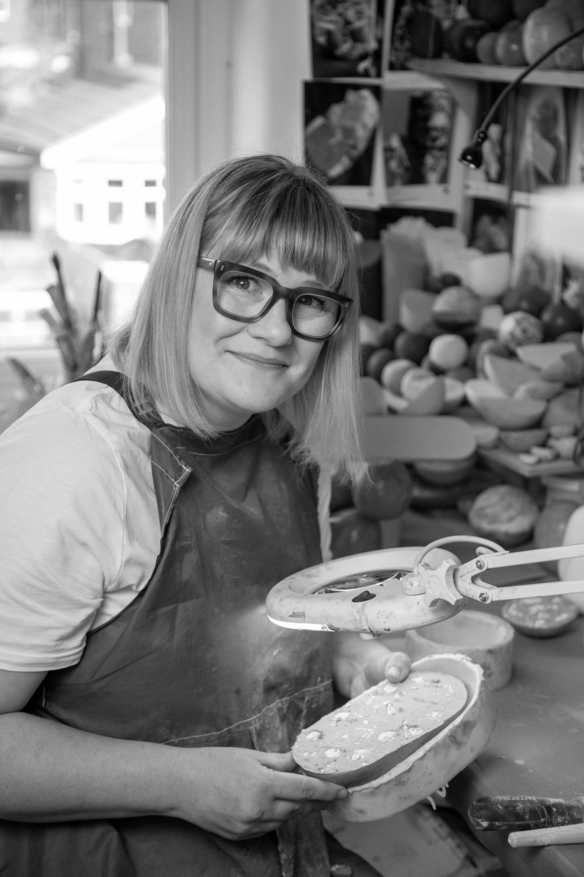 Vic Wright smiles while working on a creative project in her art studio, surrounded by colorful materials and tools.