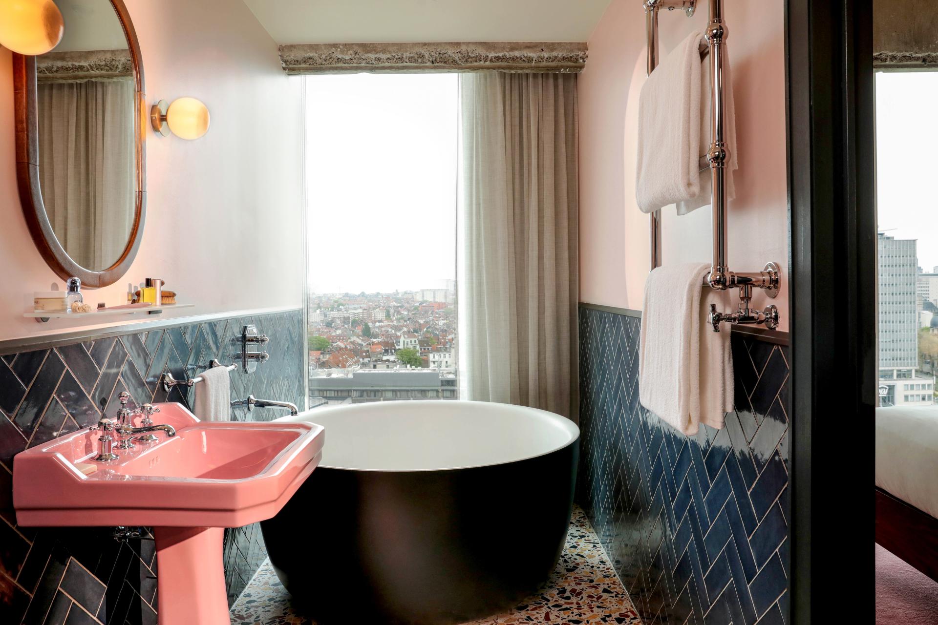 A luxurious bathroom featuring a pink sink, black freestanding tub, and stylish blue herringbone tiles.