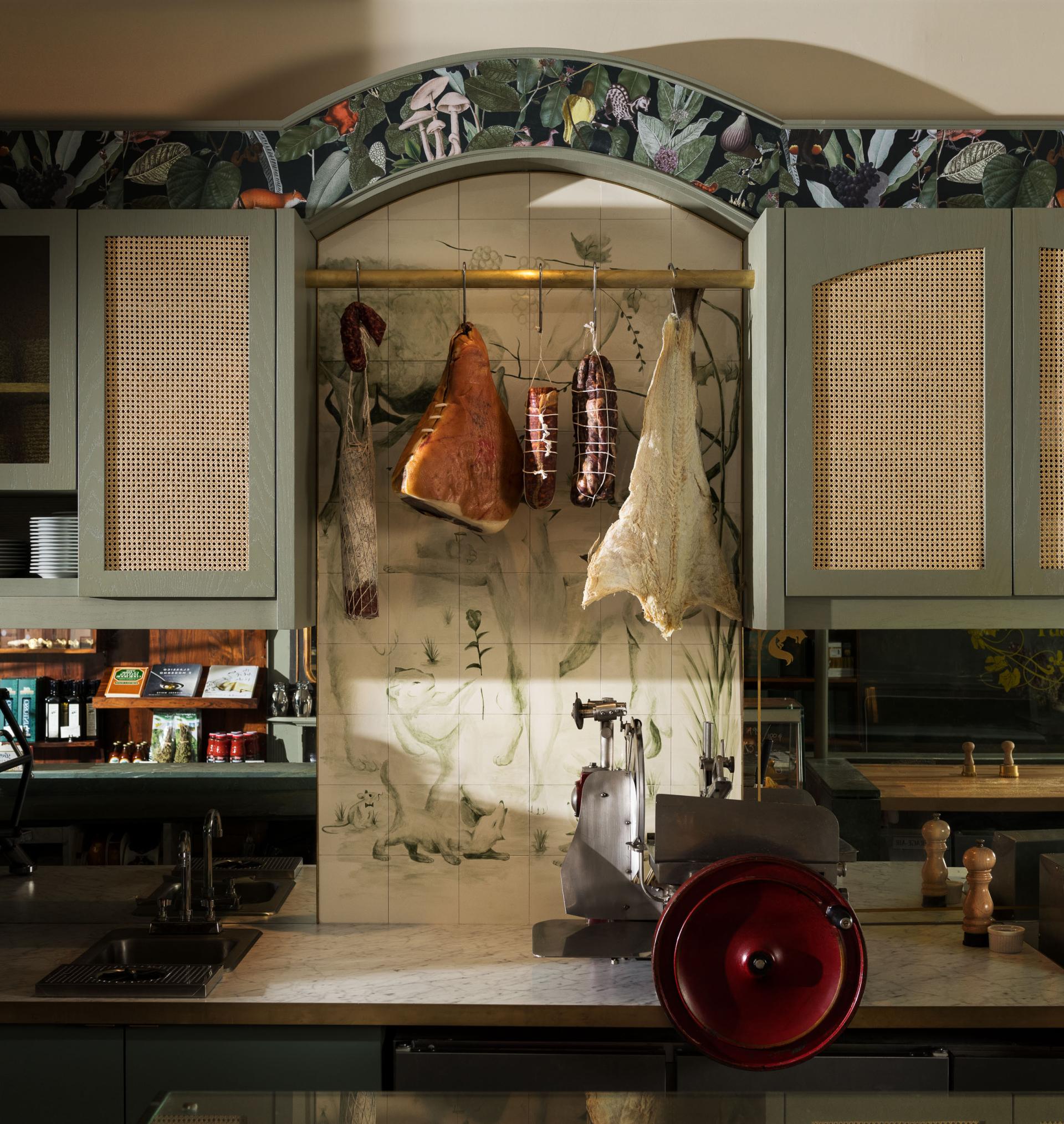 Hanging cured meats and vintage kitchen equipment showcase old-world Italian charm in Caffè La Tana's inviting design.