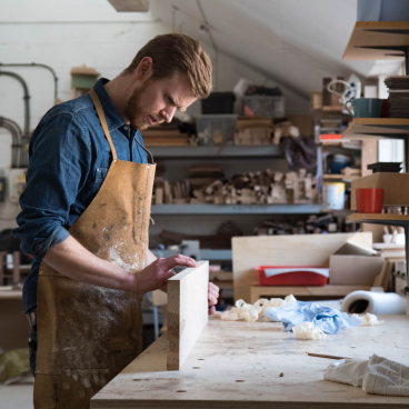 Craftsman in a workshop focusing on woodworking, surrounded by tools and materials in East London, emphasizing craftsmanship and design.