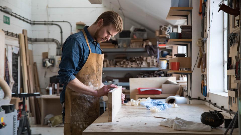 Craftsman in a workshop focusing on woodworking, surrounded by tools and materials in East London, emphasizing craftsmanship and design.