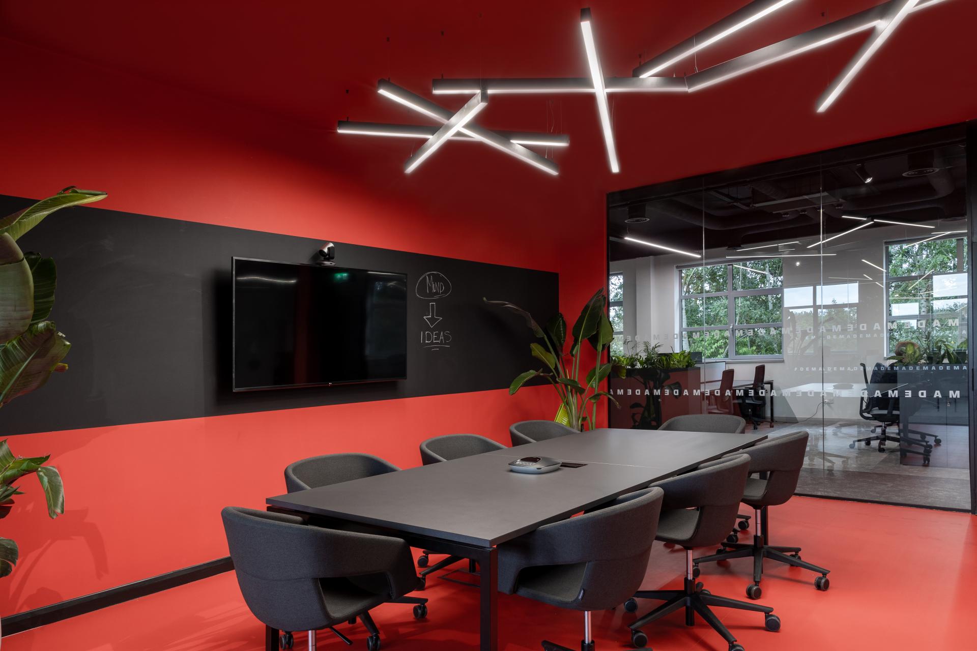 Modern conference room at M1NT Studio featuring sleek furniture, vibrant red walls, and a large screen for collaboration.