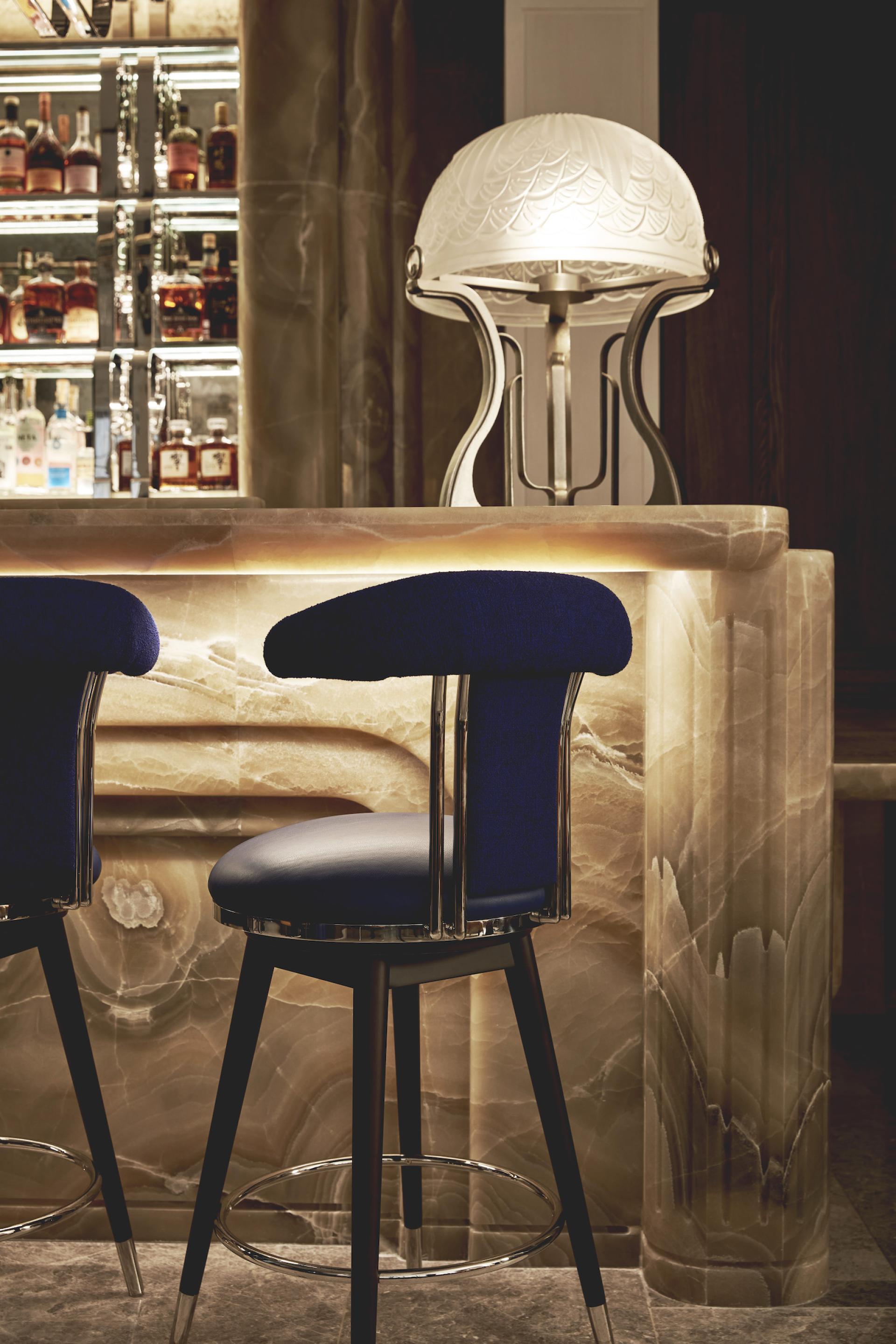 Elegant bar with Art Deco styling, featuring a marble counter, plush blue stools, and stylish lighting.