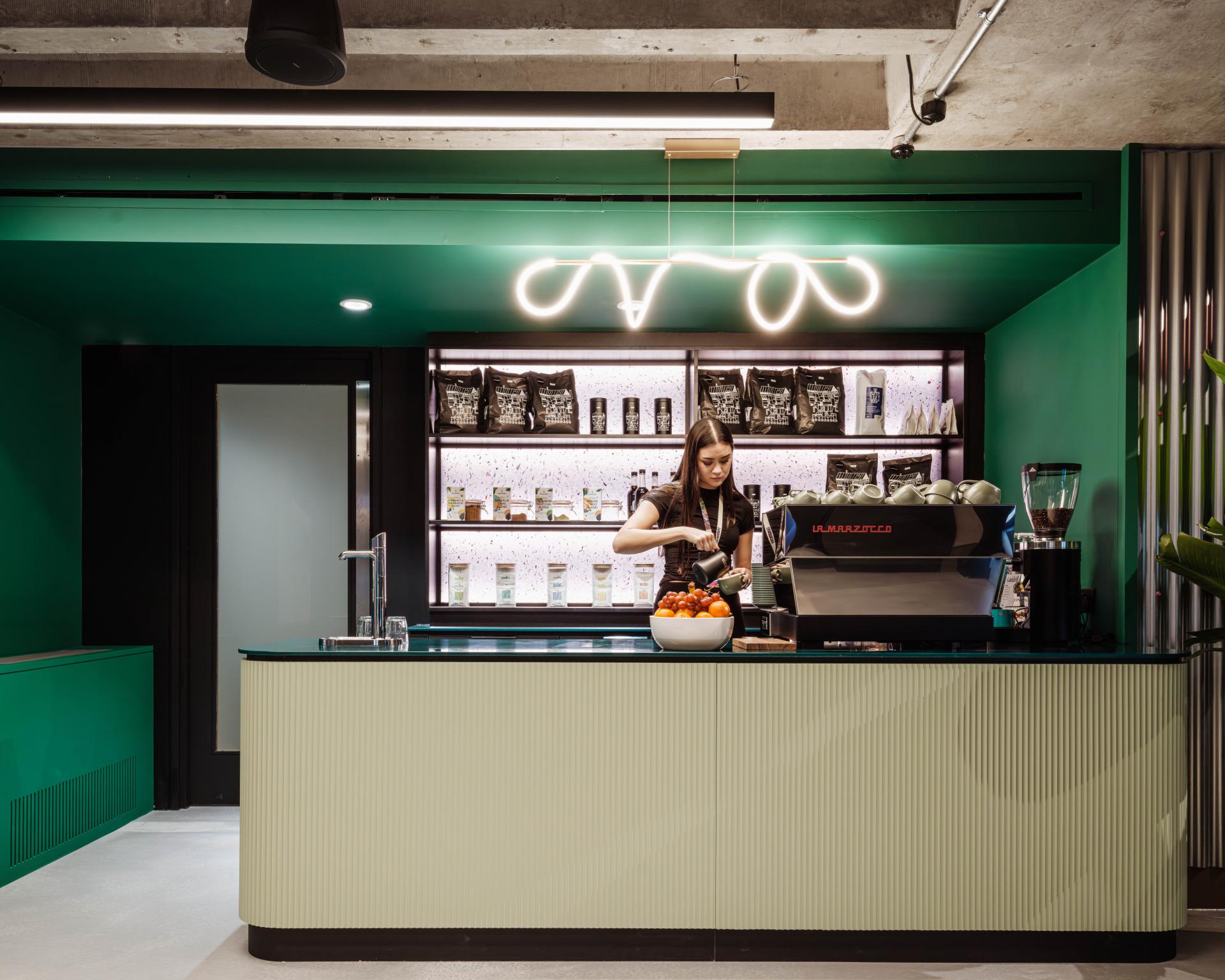 Modern coffee bar at Huckletree Kensington showcasing vibrant green hues and a sustainable layout, featuring fresh produce and equipment.