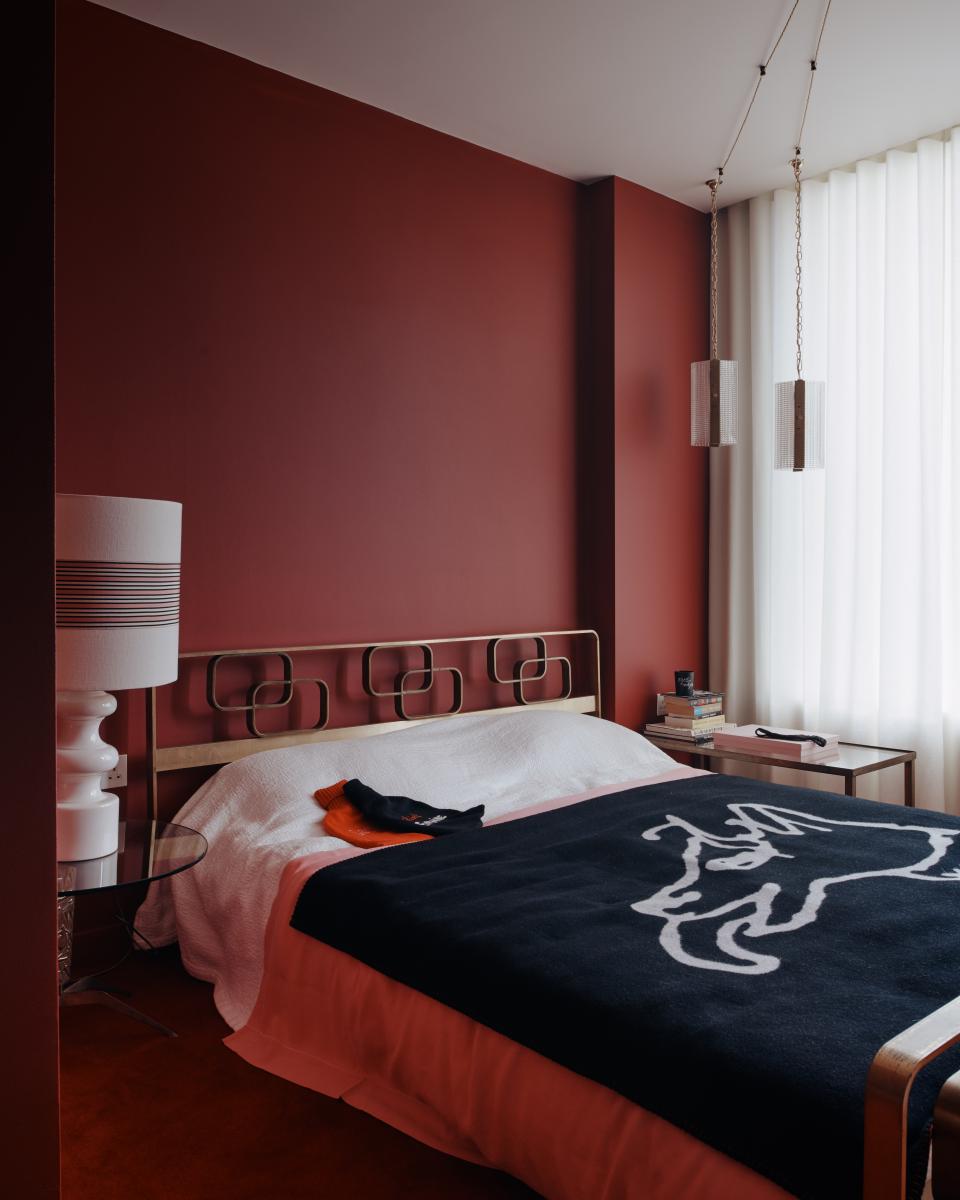 Elegant bedroom designed by Bella Freud and Maria Speake, featuring a red wall, stylish bedding, and contemporary decor.