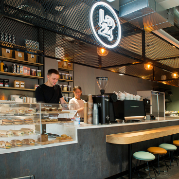Stylish café interior featuring staff serving drinks and pastries, showcasing contemporary design and a client-centered atmosphere.