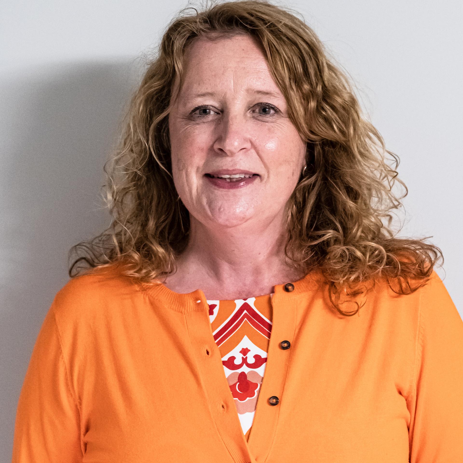 Professional woman with curly hair, wearing an orange cardigan, discussing Manchester’s property sector and co-living trends.