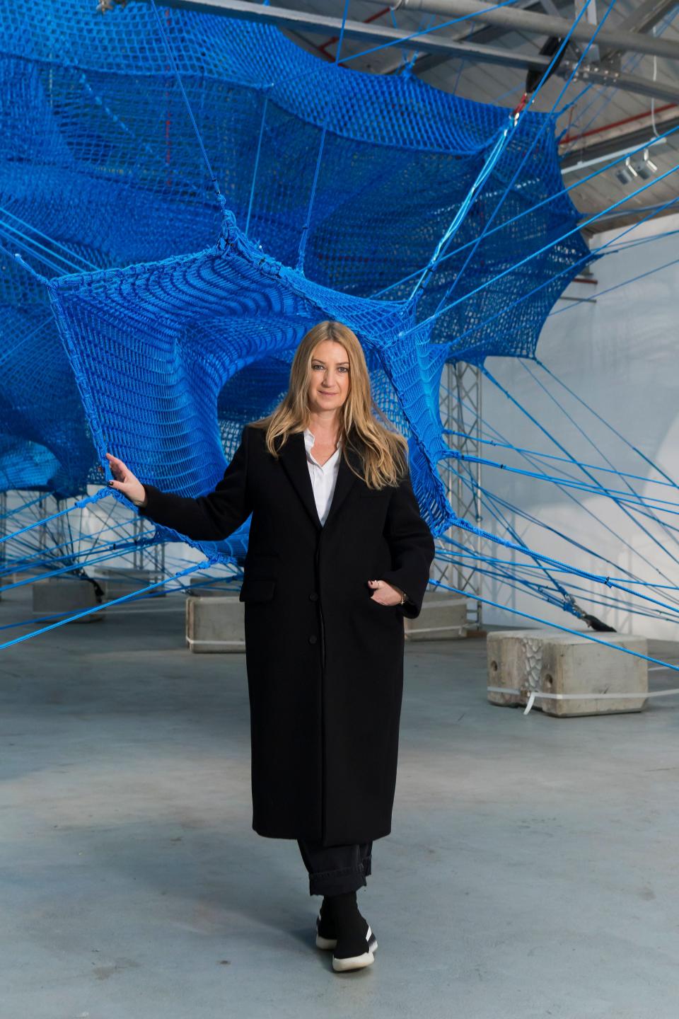 Anya Hindmarch stands in her immersive Weave Project installation, surrounded by vibrant blue netting and structural elements.