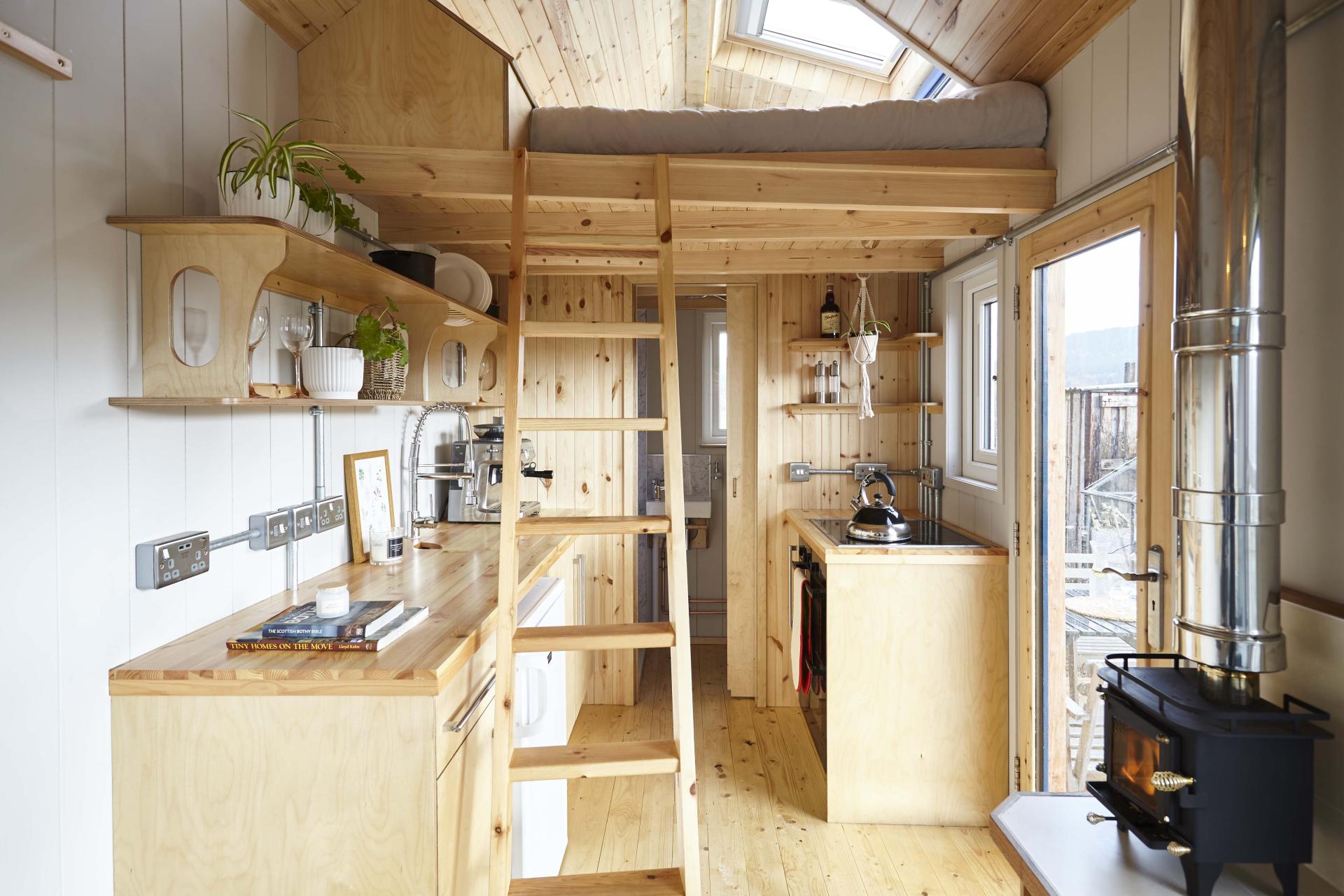 Interior view of a stylish, wooden tiny house showcasing modern kitchen design and a loft sleeping area.