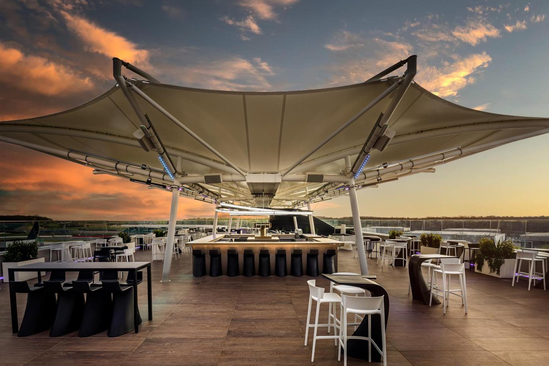 Contemporary rooftop restaurant with stylish seating and elegant canopies, showcasing harmonious architecture against a sunset backdrop.