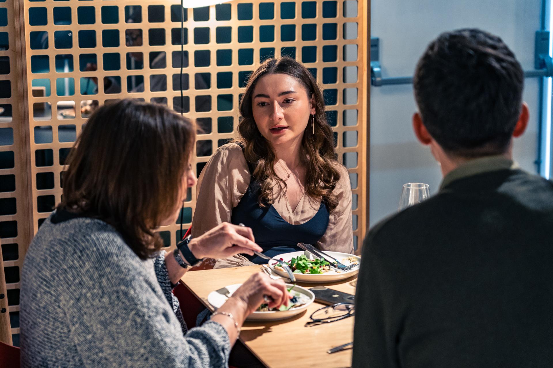 Three people engaged in a discussion over a meal, emphasizing collaboration for achieving Net Zero sustainability goals.