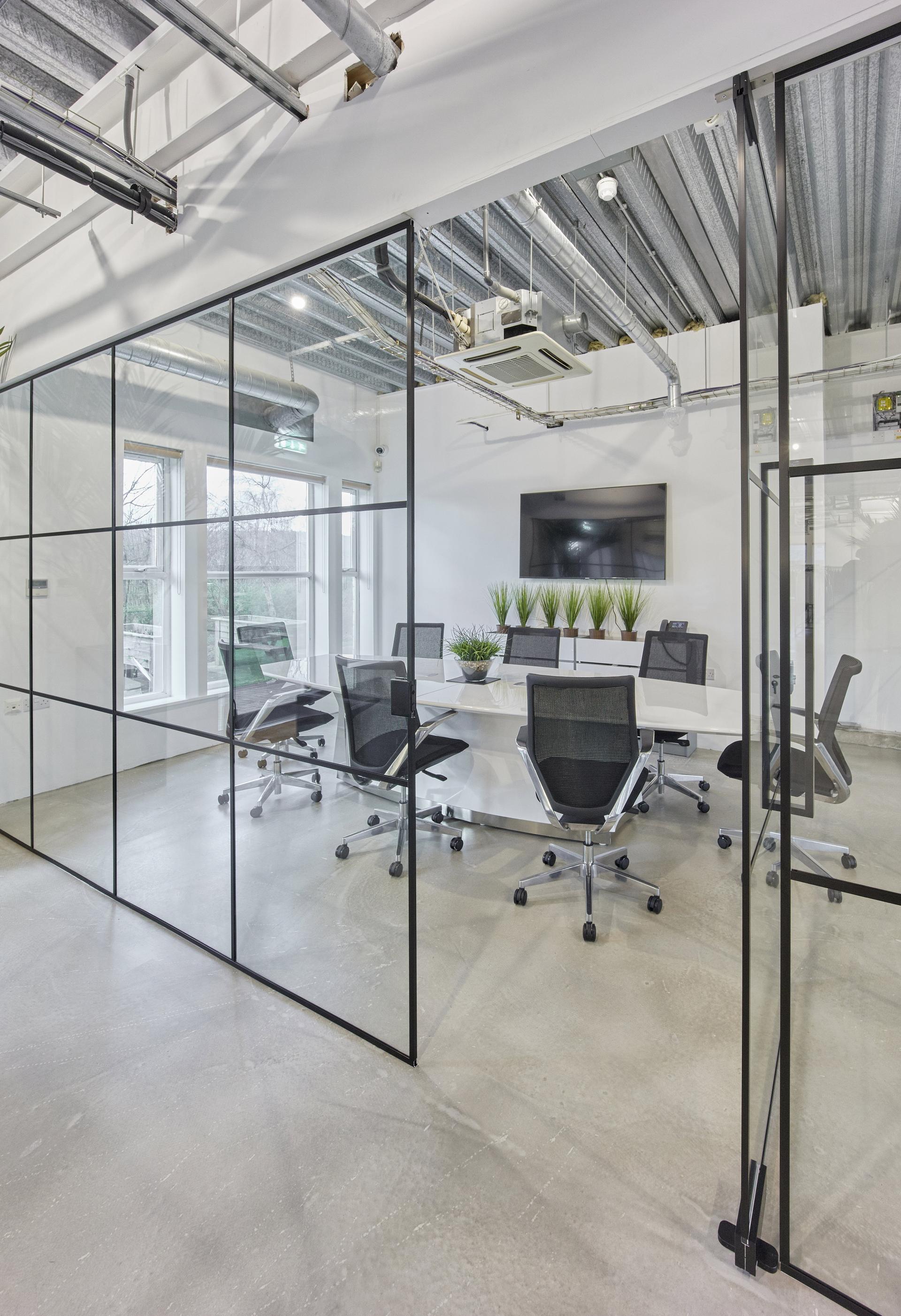 Modern meeting room with glass walls, sleek black chairs, and plants, enhancing the workspace at MKI HQ.