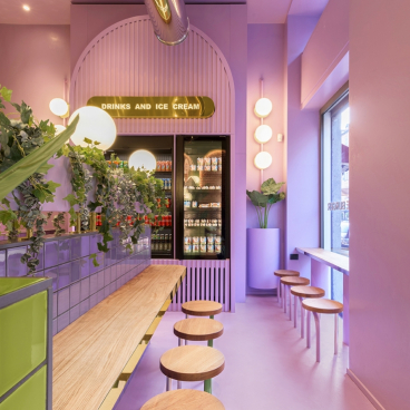 Stylish ice cream shop interior featuring vibrant purple hues, greenery, and modern seating arrangements, showcasing innovative hospitality design.