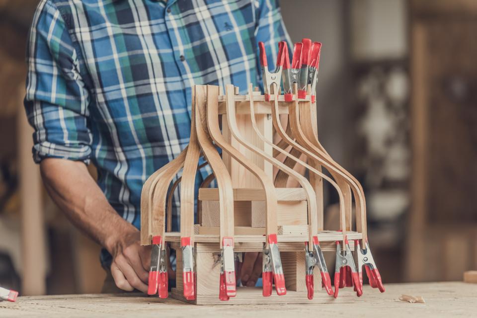 Craftsman shaping wooden lampshade components, secured with clamps, inspired by art deco design techniques.