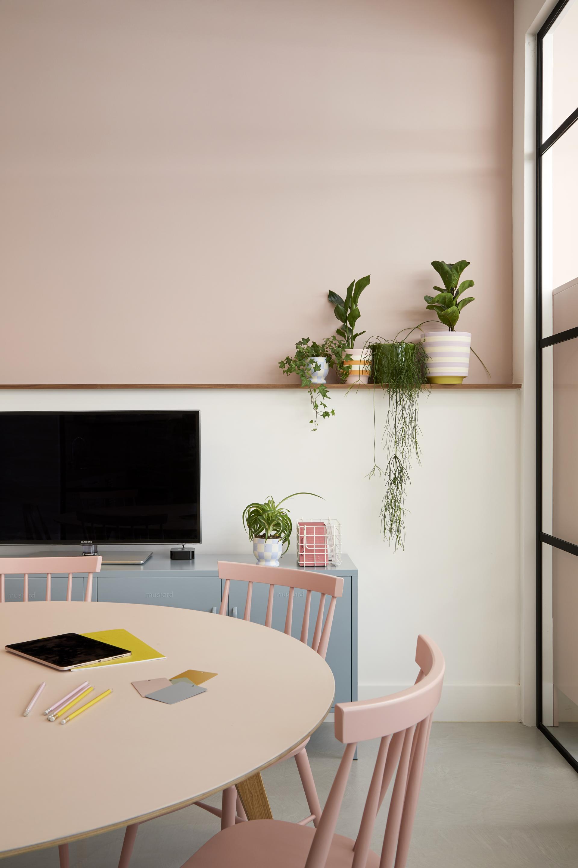 Brightly colored workspace featuring a round table, pink chairs, plants, and modern decor reflecting Mustard Made's creative vision.