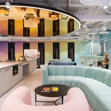 Vibrant coworking space featuring colorful furniture, a communal kitchen area, and guests engaging in a creative environment.