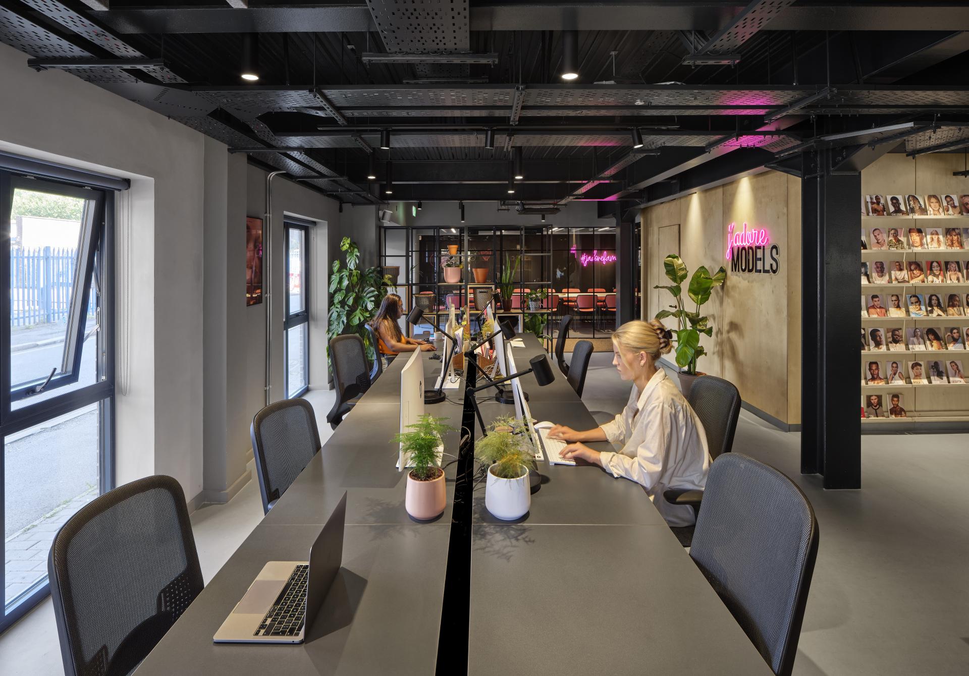 Modern office interior of J’adore Models, showcasing sleek desks, potted plants, and stylish decor in a bright workspace.
