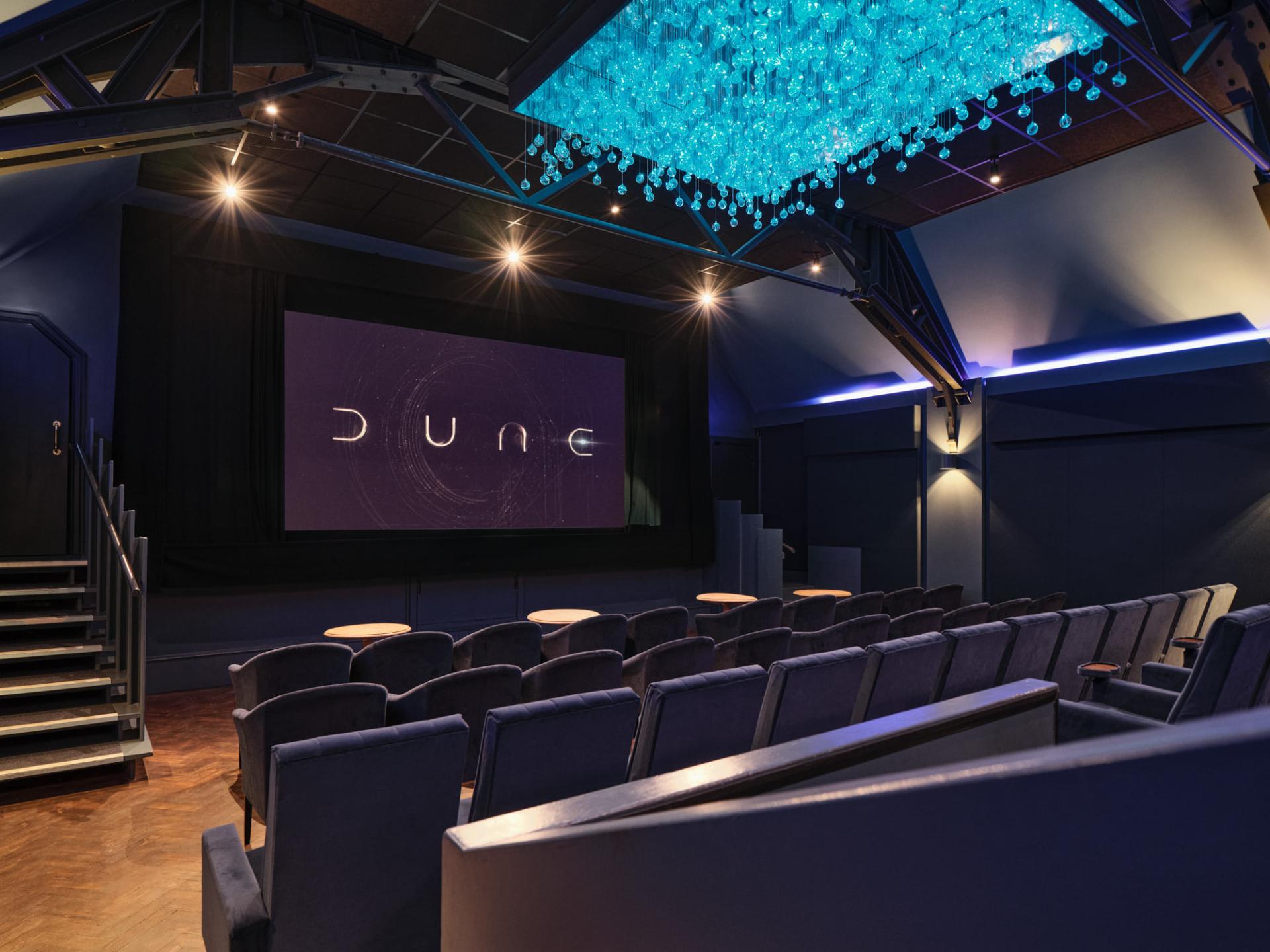 Refurbished cinema interior featuring a large screen showing "Dune" with elegant blue lighting and comfortable seating.
