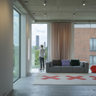 Modern studio interior featuring floor-to-ceiling windows, contemporary furniture, and a view of Amsterdam's skyline, designed by thonik.