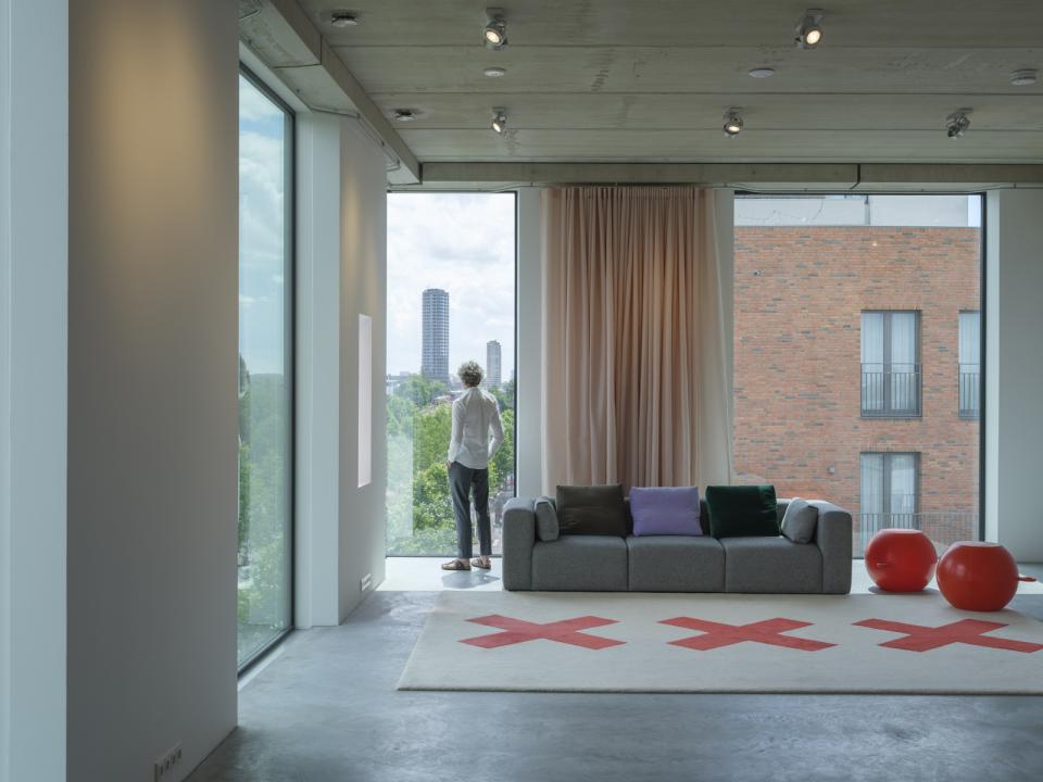 Modern studio interior featuring floor-to-ceiling windows, contemporary furniture, and a view of Amsterdam's skyline, designed by thonik.