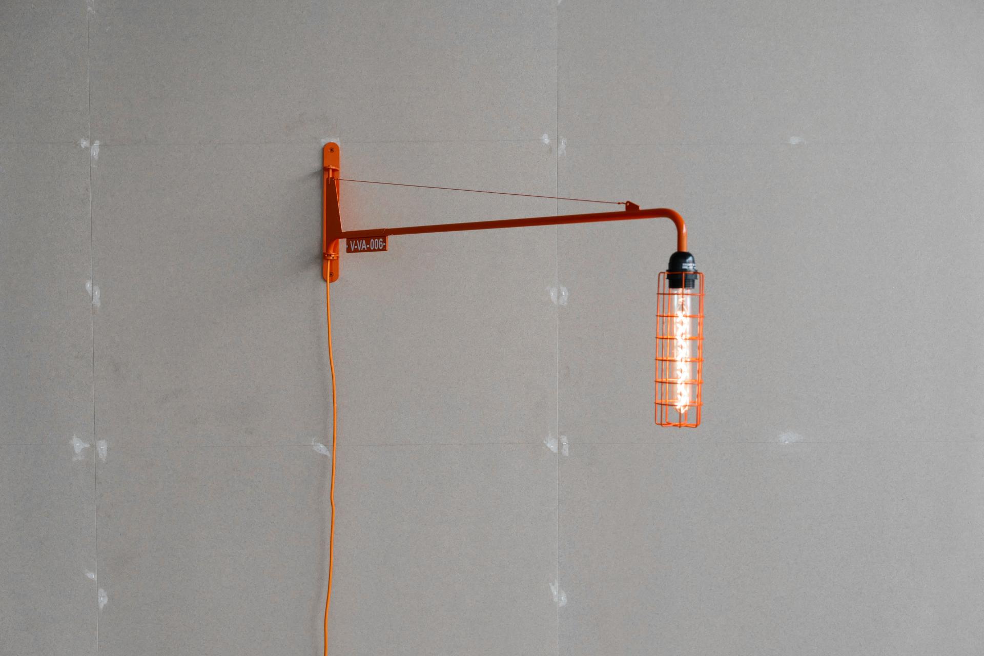 Vitra's innovative wall lamp designed by Virgil Abloh features a striking orange frame and vintage-style bulb.