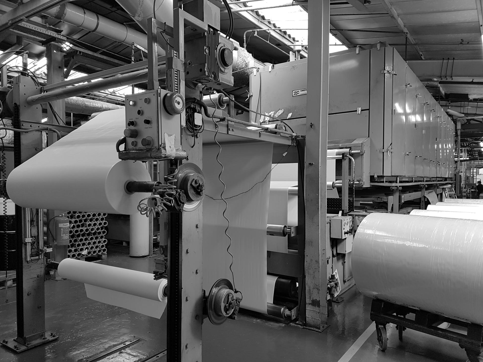Industrial machinery in Muraspec's factory, showing large rolls of coated wallpaper in production process.