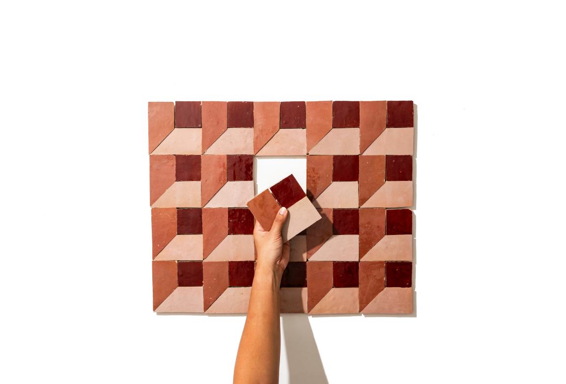 Colorful zellige tiles arranged in geometric patterns, with a hand placing a tile into a design.