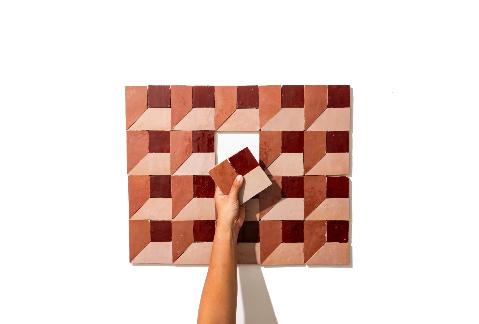 Colorful zellige tiles arranged in geometric patterns, with a hand placing a tile into a design.